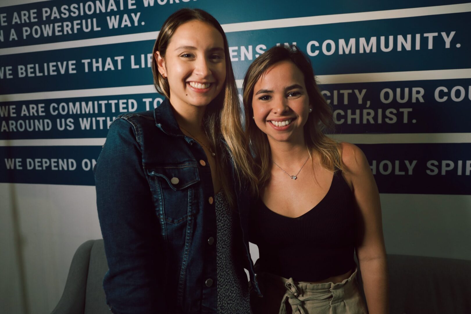 Two women posing for a picture in front of a wall.